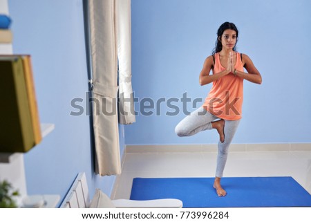 Pretty young woman standing in tree position on yoga mat