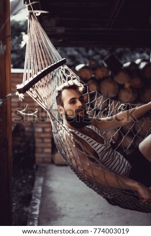 bearded man smiling, resting, lying hammock on a warm summer day. sunset sun, rest in a hammock after a hard day.
