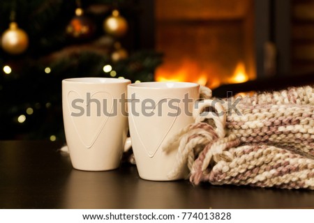 two tea mugs, knitted scarf and christmas tree and fireplace in the background - hygge concept