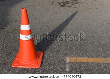 traffic cone, with white and orange stripes on gray asphalt.