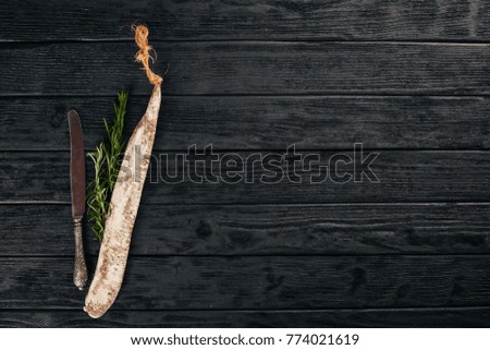 Fuet, Salami and Rosemary. Traditional Spanish sausage. On a black wooden background. Top view.
