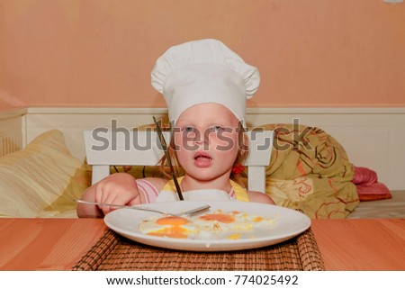 Small girl has a snack. Little girl eats ham and eggs. Cute girl dressed like a chef - white chef costume. Family and childhood concept