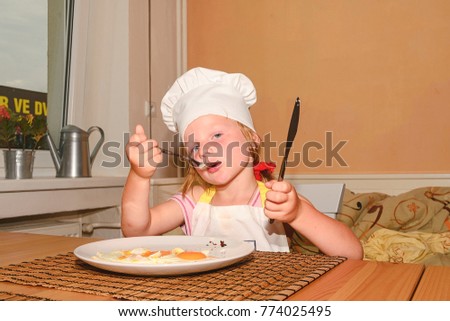 Small girl has a snack. Little girl eats ham and eggs. Cute girl wears white chef costume.  Family and childhood concept