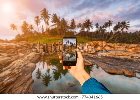 Photographing with smartphone in hand. Travel concept. Sunset on a tropical beach.