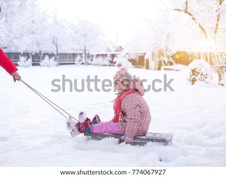 
a small child on a sled. girl rolls on snowdrifts in winter, sun shines