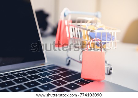 Shoping online concept, Colorful paper shopping bag in trolley on laptop. Customer can buy everthing from office or home and the messenger will deliver. Royalty-Free Stock Photo #774103090