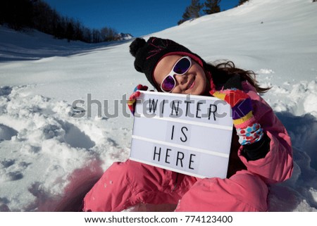 Slogan "winter is here" held by a girl in a snowy landscape.