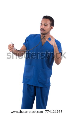A scared doctor wearing blue uniform, and stethoscope is looking at the diaphragm part of a stethoscope while putting the earpieces in his ears. Isolated on white background.