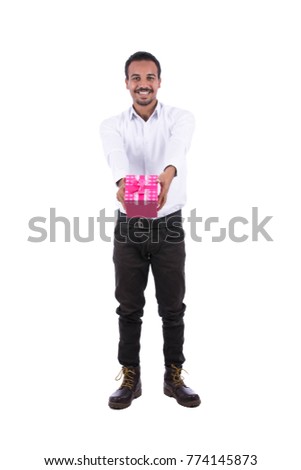Full-length image of a cheerful guy wearing white shirt, black trousers, and boots giving Christmas gift. Isolated on white background.
