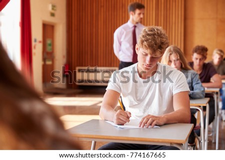 Teenage Students Sitting Examination With Teacher Invigilating Royalty-Free Stock Photo #774167665