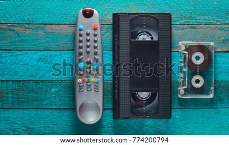 Video cassette, audio cassette, remote control on a turquoise wooden table. Retro media technology from the 80s. Copy space. Top view.