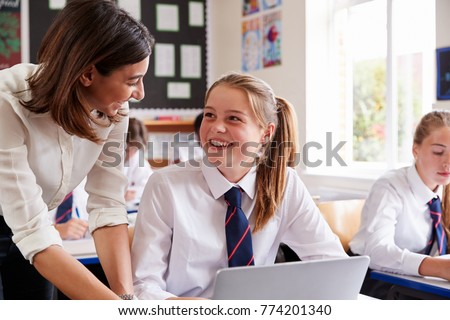Female Teacher Helping Pupil Using Computer In Classroom Royalty-Free Stock Photo #774201340