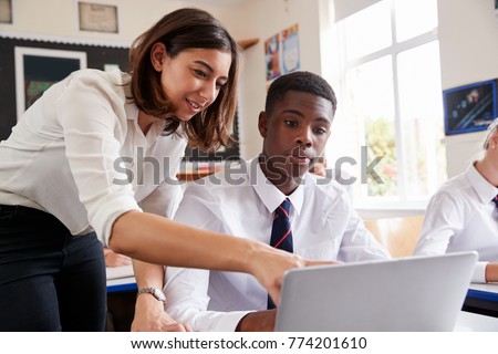 Female Teacher Helping Pupil Using Computer In Classroom Royalty-Free Stock Photo #774201610