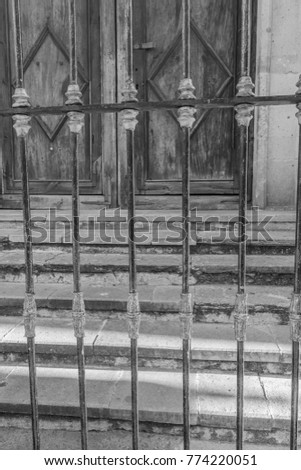 Iron Gate-close-up of a decorative iron gate, with stone steps and aged wooden double doors in the background, in black and white