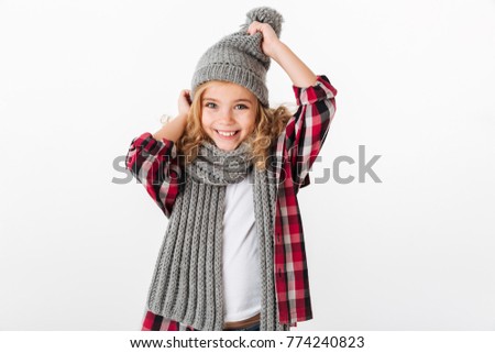 Portrait of a cheery little girl dressed in winter hat and scarf posing and looking at camera isolated over white background