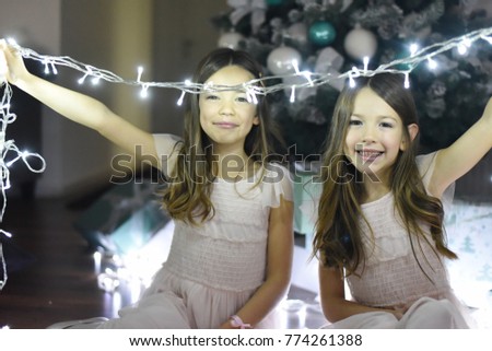 Two little girls play with Christmas lights. Portrait of beautiful girls enjoy in holidays together. 