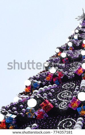 A fragment of a huge Christmas tree with many ornaments, gift boxes and luminous lamps. Photo of a decorated Christmas tree close-up with copy space