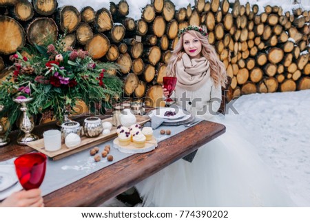 Cheerful bride is holding a wine glass, sitting on the decorated table. Selective focus on the girl. Winter wedding