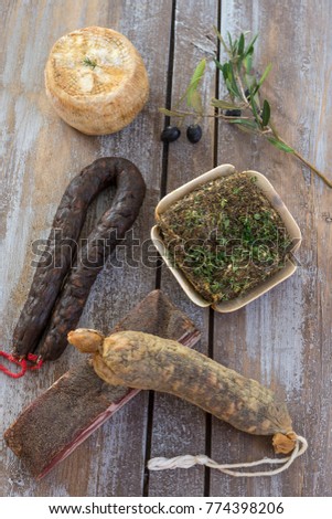 several variety of traditional Corsican charcuterie on a wooden background with an olive branch and black olives