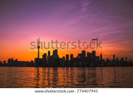 FLIGHT ARRIVING IN TORONTO - Popular international travel, tourism and immigration destination in Canada. Downtown business buildings at sunset with airplane flying into city. Purple, orange color sky