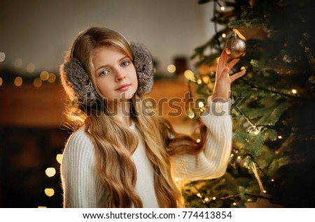 Close up portrait  of beautiful young girl with long curly blonde hair on a christmas background with boke lights. Magic warm new year photo.Cozy interior.