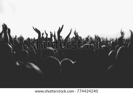 Black and white picture of huge crowd of people with the hands raised up on a big music show