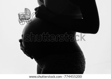 tummy of a pregnant woman in silhouette with a decorative stroller