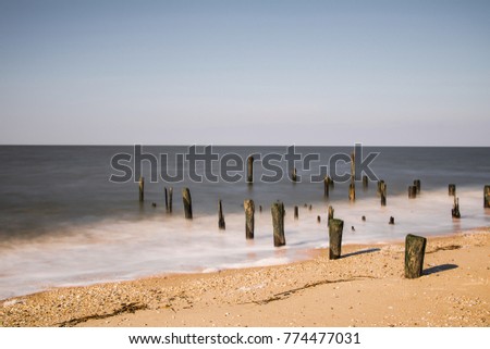 Exterior daytime long exposure stock photo of wooden pylons rising from sand on Cape May, New Jersey beach in Cape May County on Delaware Bay while waves come in on winter December afternoon