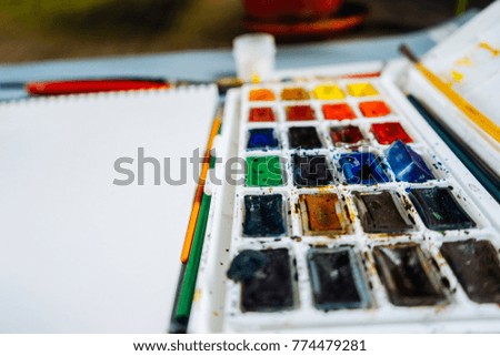 on the table are the artist's accessories, colorful watercolors, brushes and pencils