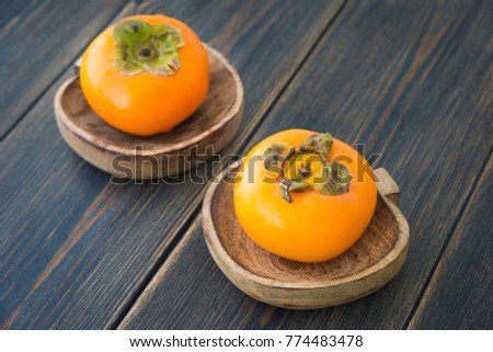 Fresh ripe solid persimmons in wooden plates on dark rustic wooden background