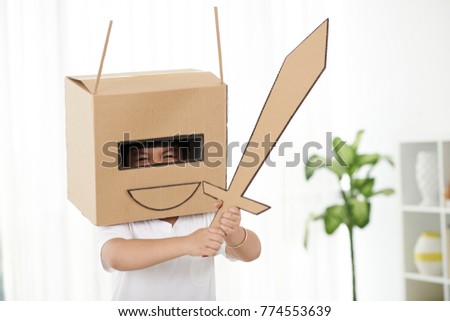 Little boy playing in carbord helmet with sword in his hands