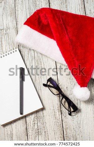 Christmas and New Year background with red Santa hat, glasses, notepad and pen for your wishes.