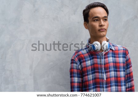 Portrait of young handsome Indian man against concrete wall in the streets outdoors
