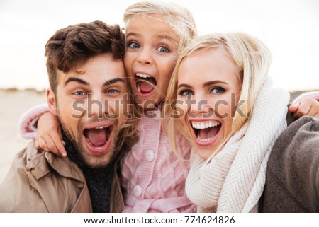 Portrait of an excited family with a little daughter taking a selfie together while standing at the beach