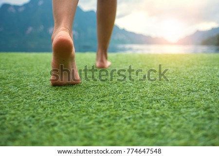 Young female legs walking towards the sunset on a ground grass with blur mountain and lake Royalty-Free Stock Photo #774647548