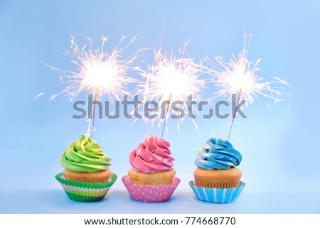 Delicious cupcakes with sparklers on light background
