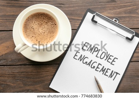 Clipboard with text EMPLOYEE ENGAGEMENT and coffee on table