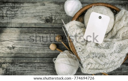 Paper label on white balls of wool threads with knitting needles into basket on vintage wooden background. Mock up background for your craft knitting logo or label