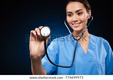 Portrait of smiling brunette caucasian doctor in blue uniform using stethoscope isolated over black