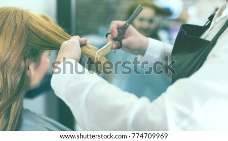 Hairdressing cutting and leveling hair to young blonde girl by means of scissors and hairbrush in salon. 