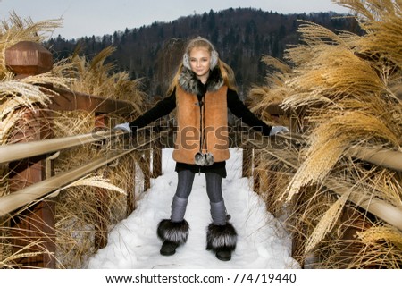 Winter fashion for kids. Cute little girl on the snow in the mountains. Little girl in fashionable winter clothing. 