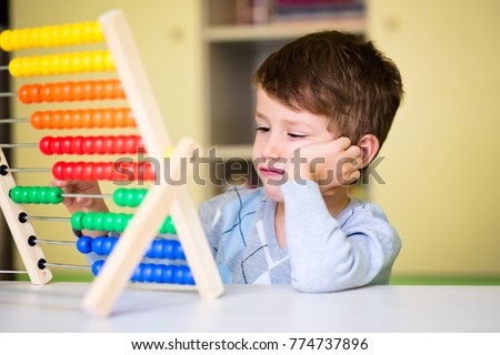 Toddler boy feeling bored and tired while playing with abacus at kindergarten. Hyperactive kid having attention deficit disorder Royalty-Free Stock Photo #774737896