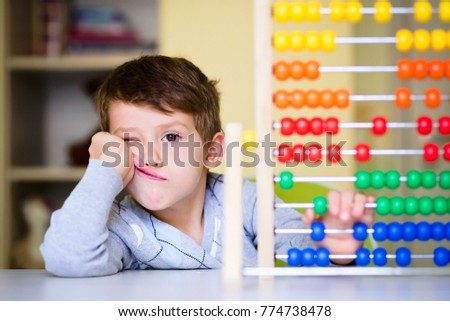 Toddler boy feeling bored and tired while playing with abacus at kindergarten. Hyperactive kid having attention deficit disorder Royalty-Free Stock Photo #774738478