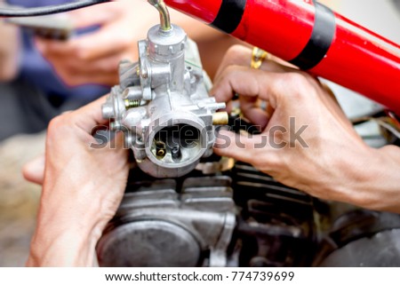 The men's hands are being repaired and picked up at the motorcycle's carburetor.
