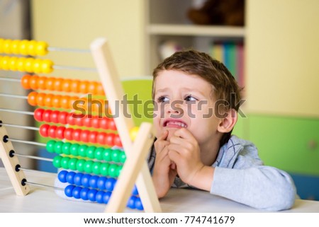 Cute toddler boy having difficulties using the abasus. Learning to count. Kids preschool activities and attention deficit. Royalty-Free Stock Photo #774741679