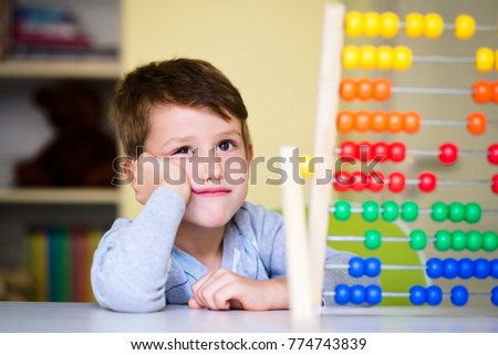 Adorable Toddler boy looking tired and bored while playing with abacus at kindergarten. Child at prechool having tedious expression. Royalty-Free Stock Photo #774743839