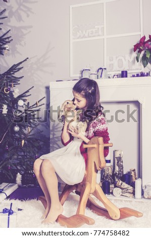 Little girl playing at Christmas tree with rabbit