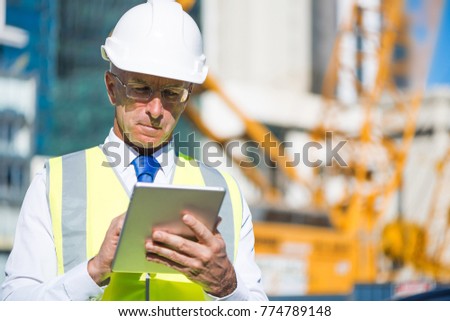Senior engineer man in suit and helmet working on tablet pc