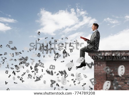 Young businessman sitting on building top with red book in hands