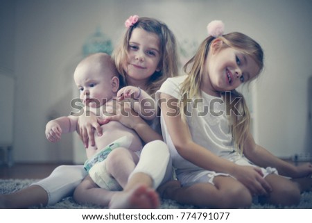 Two sisters poses to camera with baby brother. Close up. 